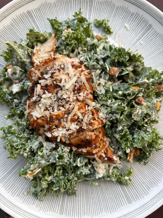 "Plate of kale Caesar salad with creamy dressing, Montreal Red grilled chicken breast topped with shaved Parmesan and black pepper