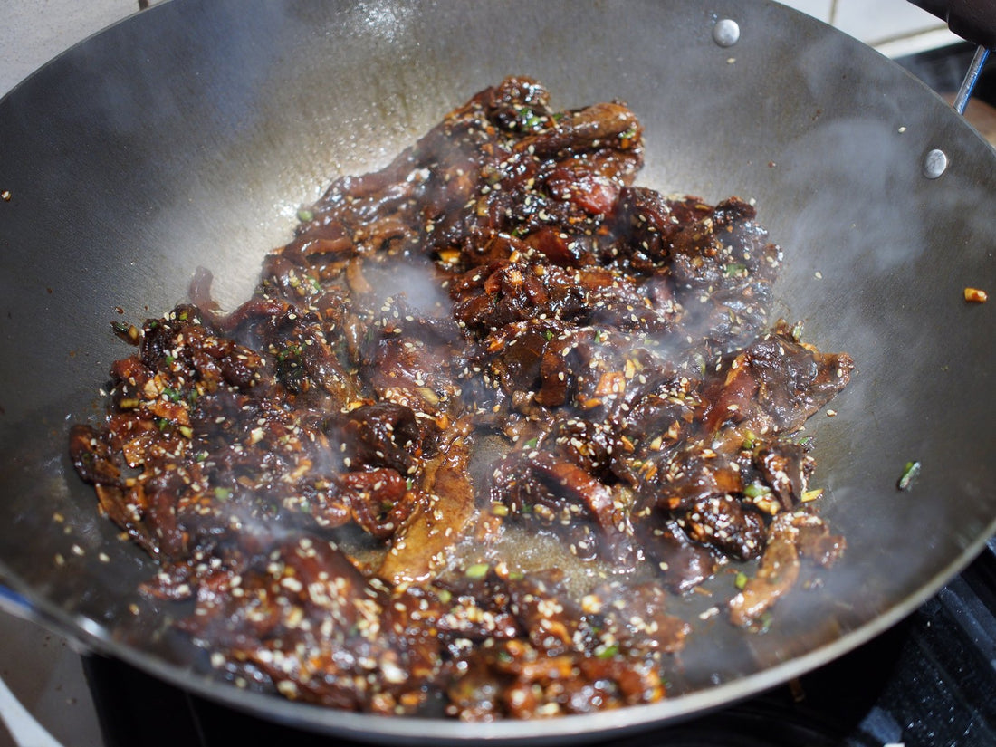 a plate of bulgogi on rice on a wooden cutting board surrounded by Korean side dishes and chilies