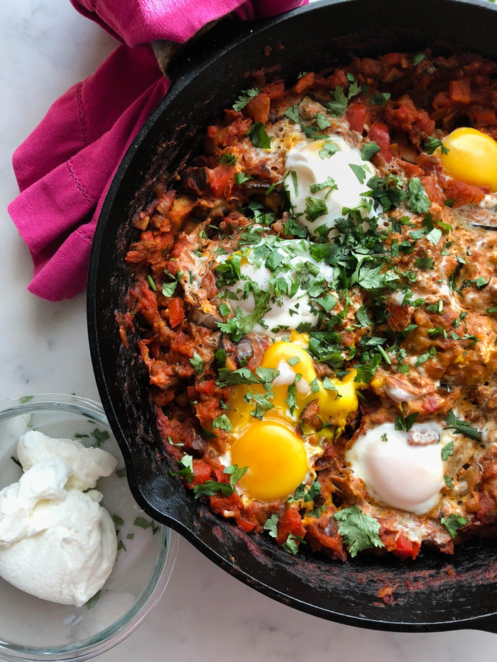 Skillet of Shakshuka with poached eggs, peppers, tomatoes, and fresh herbs