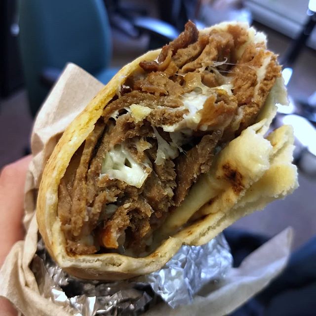 hand holding a beef shawarma wrap wrapped in napkins and tinfoil 