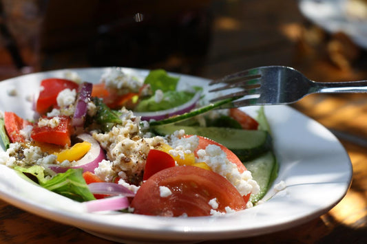 salad in a white bowl with a fork, topped with feta and greek salad dressing 