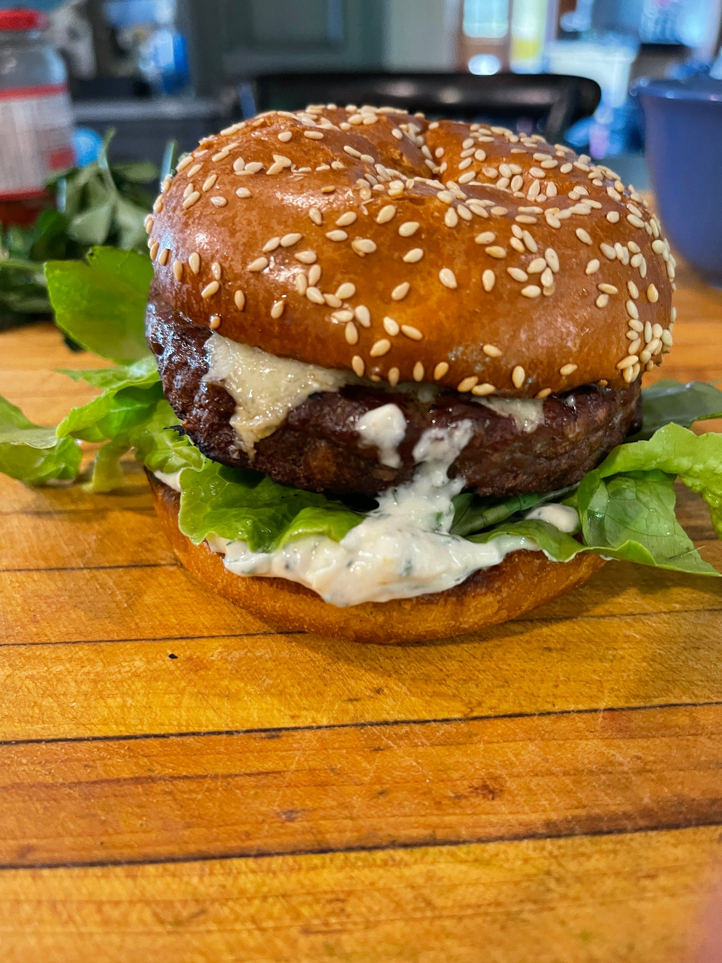 cheese burger on a golden sesame seed bun with a lot of lettuce sticking out and tzitziki sauce