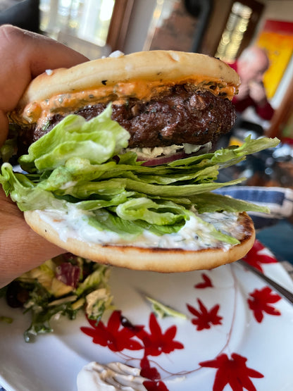 burger on flat-style buns with lots of layers of lettuce underneath with a red sauce on top and a white sauce on the bottom